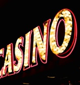 Brightly illuminated letters spell out 'CASINO' with glowing yellow bulbs and red outlines against a dark background.