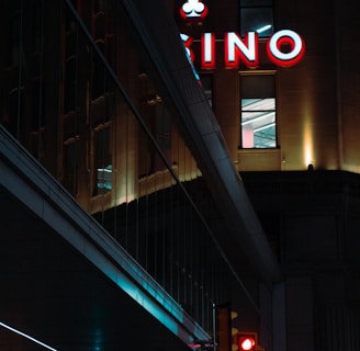 A night scene featuring a building with illuminated neon signage displaying 'CASINO'. The environment is urban with reflections on glass windows and glowing street traffic lights below. The atmosphere is dimly lit, with artificial lighting casting vibrant colors.