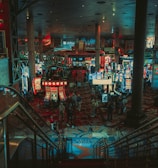 A bustling casino floor filled with groups of slot machines and people walking around. The atmosphere is vibrant with neon lights and illuminated signs. The interior has a ceiling supported by large pillars and there are stairs leading down to the gaming area.